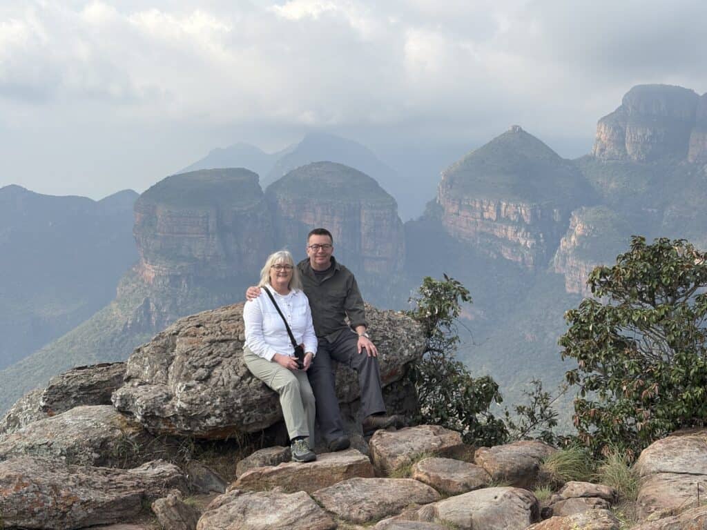 Travellers visiting South Africa photographed with the Three Rondavels of Blyde River Canyon in the background.