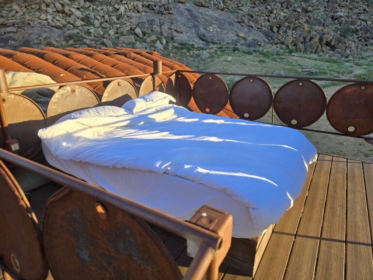 An open-air star bed overlooking the desert landscape at sunrise at Camp Sossus, Namibia.