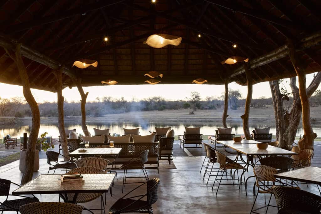 View of the dining area under a thatched structure overlooking the waterhole at Arathusa Safari Lodge in Sabi Sand, South Africa.