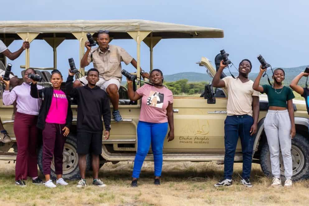 A group of students standing alongside a safari vehicle.